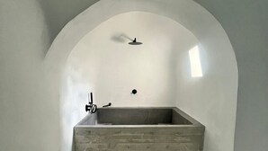 Une salle de bain minimaliste avec une grande baignoire rectangulaire, une petite fenêtre et un seul robinet.