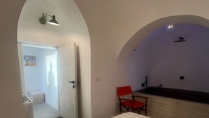 Une chambre à coucher avec un lit, une chaise rouge, un petit bureau et une salle de bain visible à travers une porte en arc de cercle.