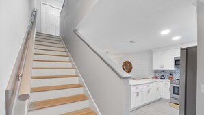 A modern kitchen with white cabinets, a stainless steel refrigerator, and a wooden staircase. - Summer Lake 15- Shore to Please (Miramar Beach)
