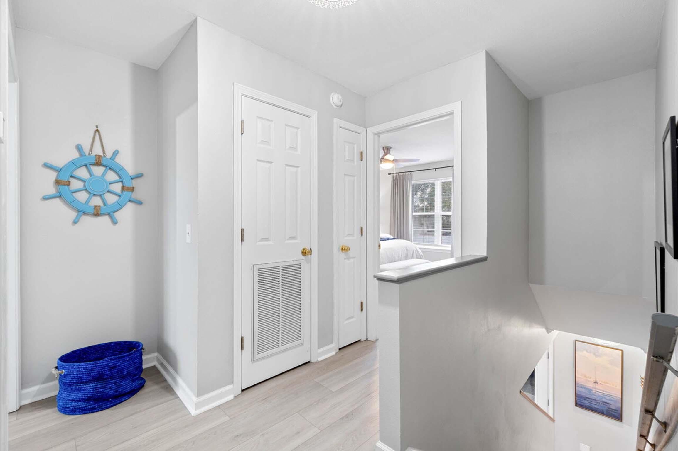 A hallway with white doors, a blue ship wheel decoration, and a framed picture on the wall.