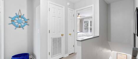 A hallway with white doors, a blue ship wheel decoration, and a framed picture on the wall.
