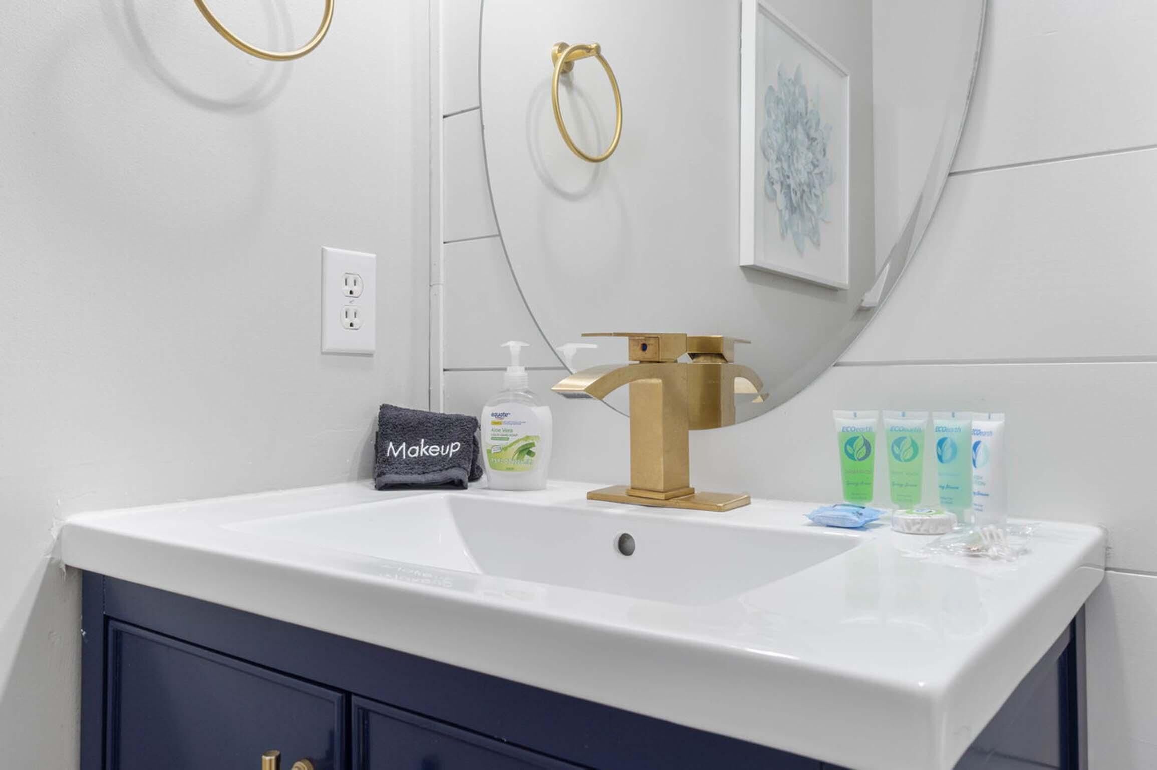 Un bagno con lavandino bianco, rubinetto dorato e una borsa per cosmetici. Sul ripiano ci sono tre flaconi verdi.