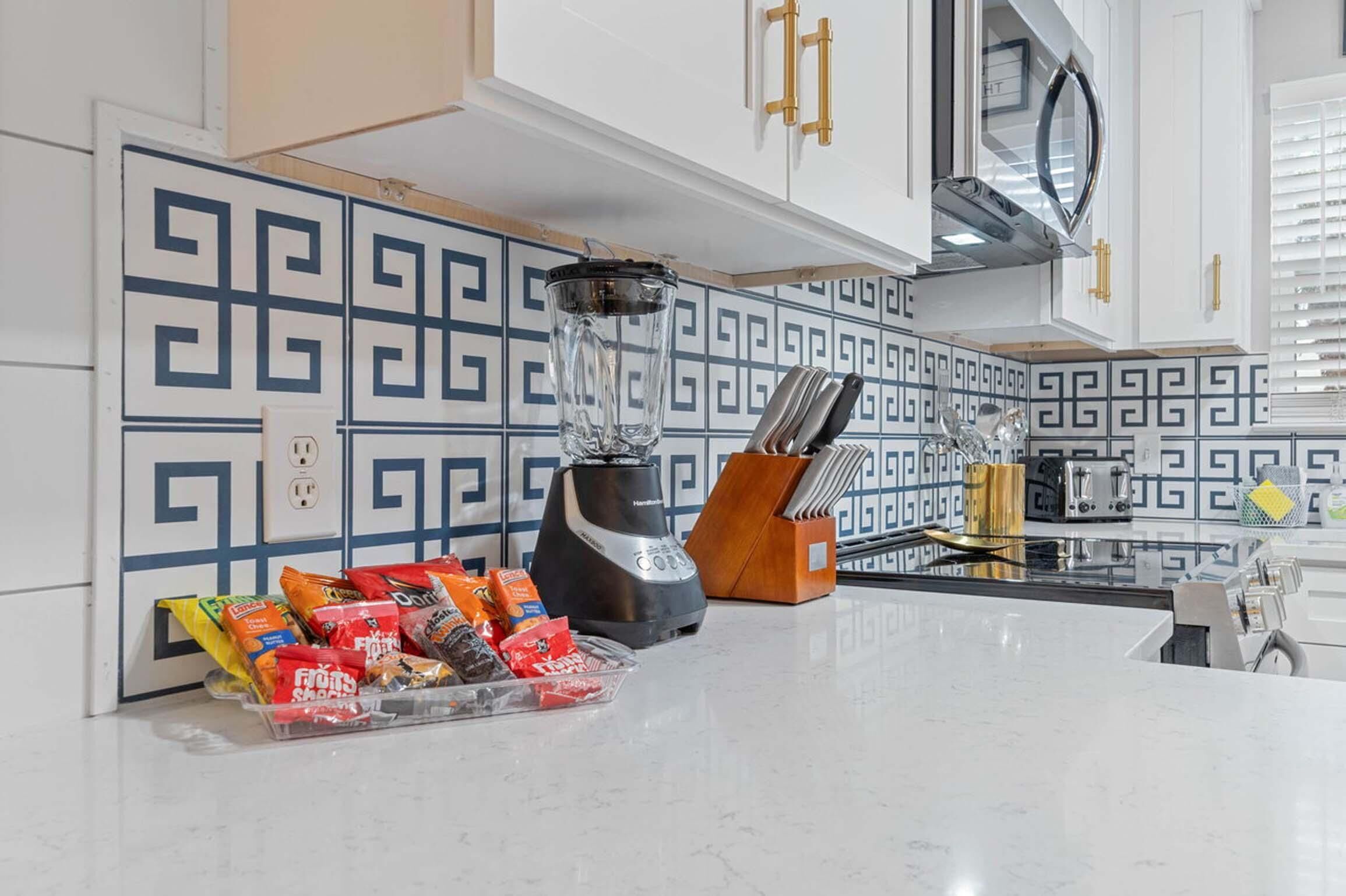 A kitchen with a modern design, featuring a blender, a knife block, and various snacks on the counter.