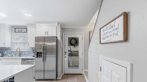 A modern kitchen with white cabinetry, a stainless steel refrigerator, and a decorative wreath on the door. - Summer Lake 15- Shore to Please (Miramar Beach)