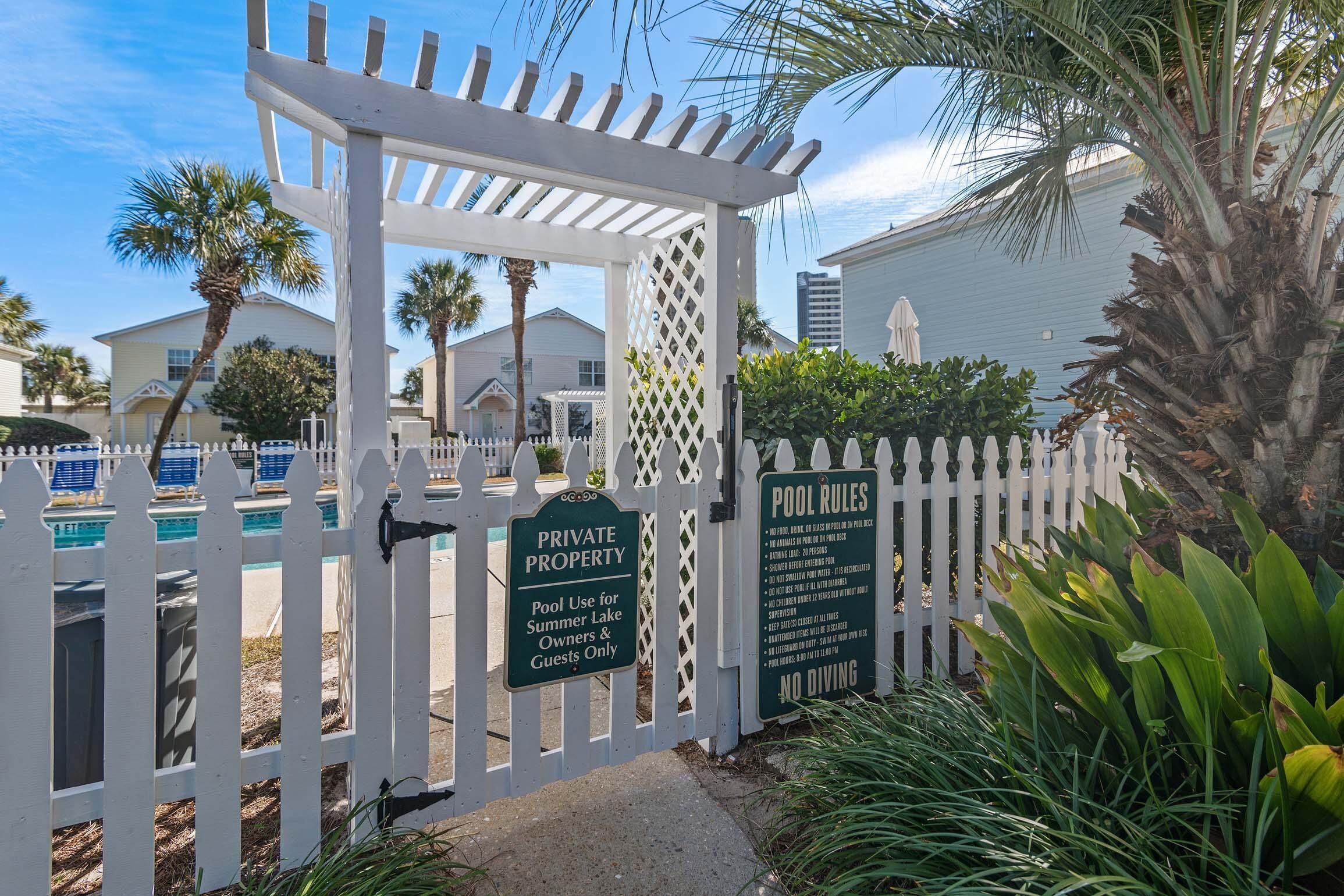 A gated pool area with a pergola, palm trees, and a sign indicating it is private property for summer lake owners and guests.