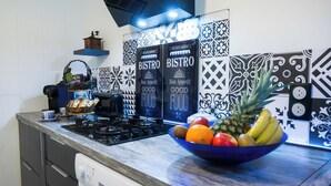 A kitchen with a gas stove, a bowl of fruit, and patterned tiles on the wall.