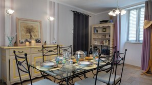 A dining area with a glass table, metal chairs, and a bookshelf with books and decorative items. - L'Ecrin Occitan (Lauraguel)