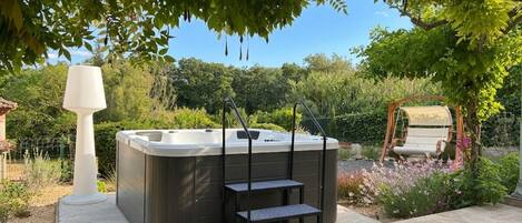 A hot tub with steps, a swing chair, and a pergola in a garden setting.