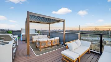 A rooftop deck with outdoor furniture, a grill, and a pergola.