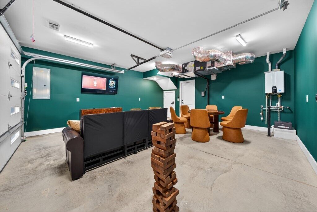 A modern, well-lit room with teal walls, a black sofa, and orange chairs. There is a large window, a white door, and a visible water heater.