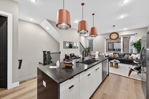 Egy modern konyha központi szigettel, függesztett lámpákkal, valamint egy étkezősarokkal, amelyben kanapé és dohányasztal található.