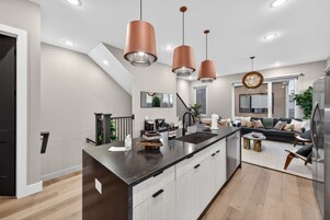 A modern kitchen with a central island, pendant lights, and a dining area with a sofa and coffee table.