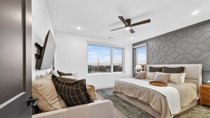 Ein modernes Schlafzimmer mit einem großen Bett, einer Couch und Blick auf die Stadt durch große Fenster.