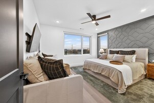 A modern bedroom with a large bed, a sofa, and a view of the cityscape through large windows.