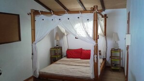 A room with a four-poster bed, red pillows, two bedside tables with lamps, and a wooden ceiling. - New! Tikanot'la haut Exceptional view of Grande Anse beach (Deshaies)