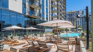 A rooftop pool area with sun loungers and umbrellas, surrounded by high-rise buildings. - Saiya  920 (Phoenix)