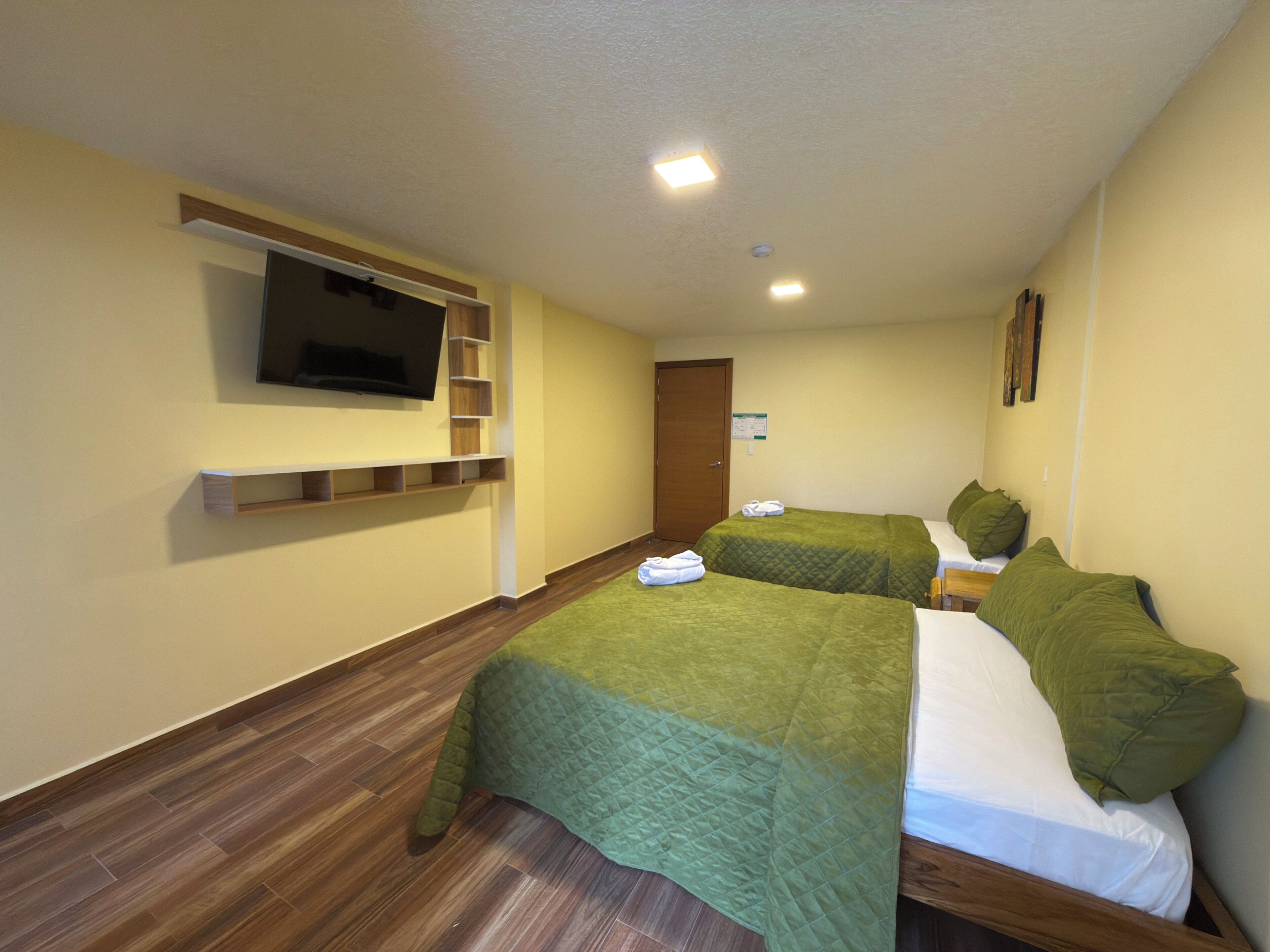 Ein Hotelzimmer mit zwei Betten, einem flachbildfernseher an der Wand und Holzboden.