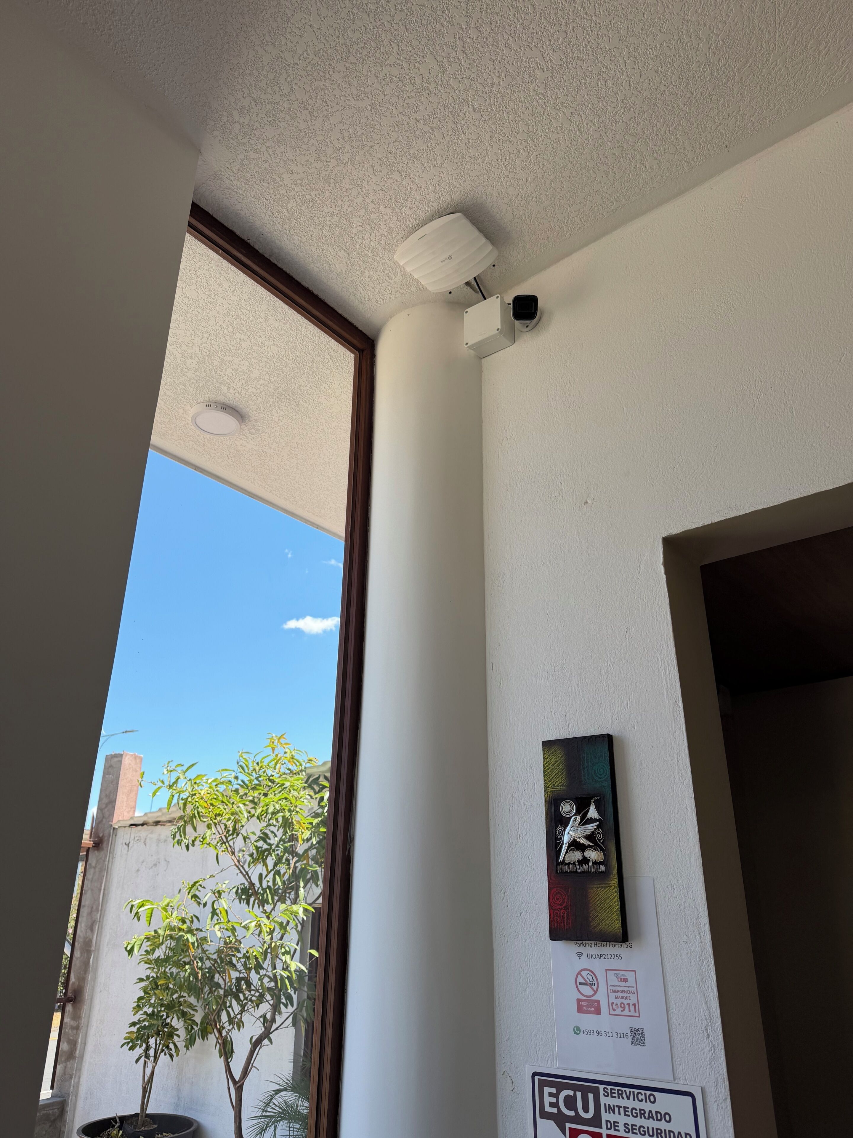 A room with a ceiling-mounted smoke detector, a security camera, and a door frame.