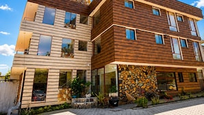 Een modern gebouw met twee verdiepingen, een stenen gevel en houten lambrisering, met meerdere balkons en grote ramen.