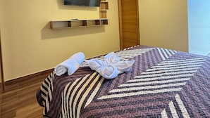Een hotelkamer met een bed, een flatscreen televisie aan de muur, een houten deur en een raam.