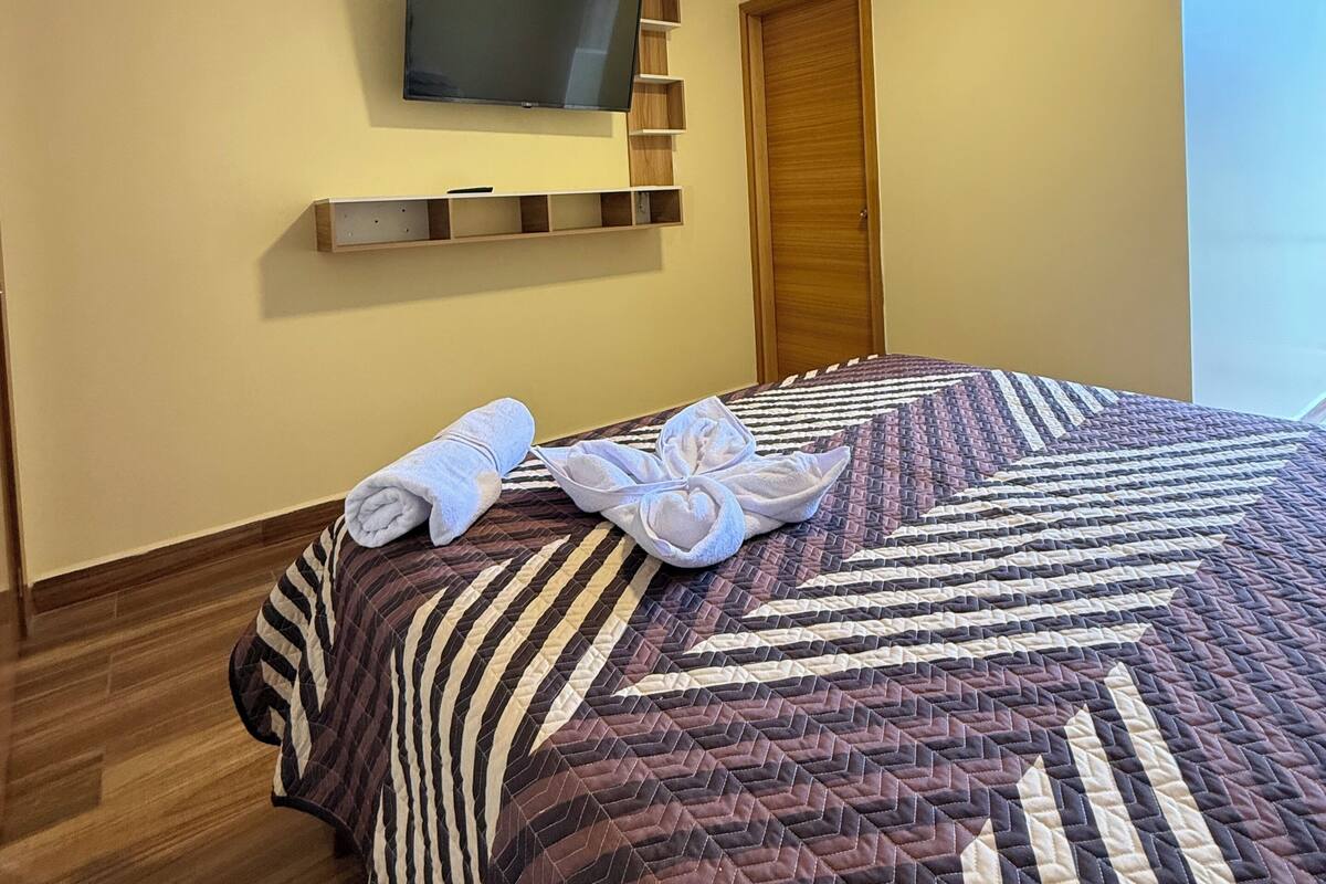 Een hotelkamer met een bed, een flatscreen televisie aan de muur, een houten deur en een raam.