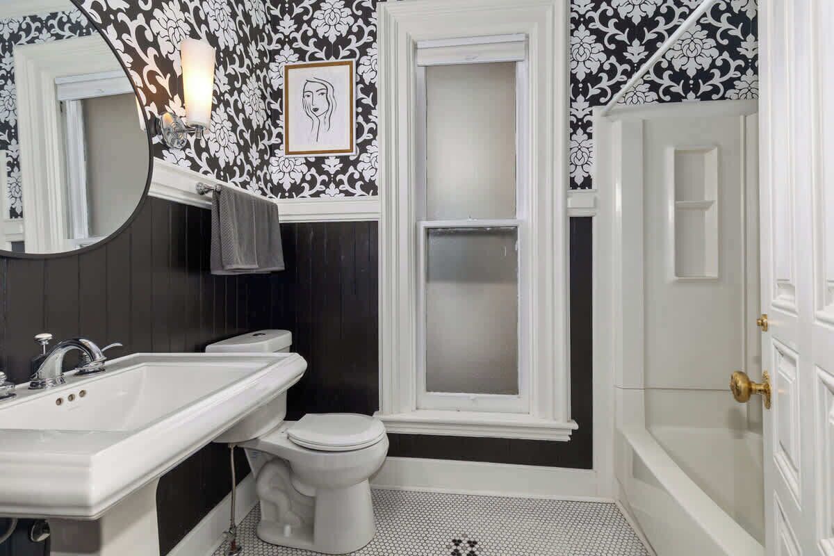A bathroom with a white sink, toilet, and bathtub. There is a window with frosted glass and a framed artwork on the wall.