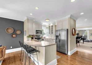 A modern kitchen with a central island, stainless steel appliances, and a dining area with a piano.