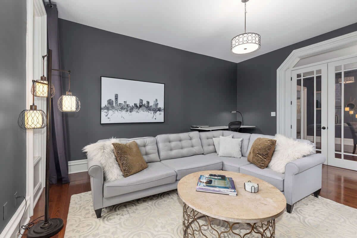 Una sala de estar moderna con un sofá seccional gris, una mesa redonda de centro y una obra de arte con un paisaje urbano en la pared.