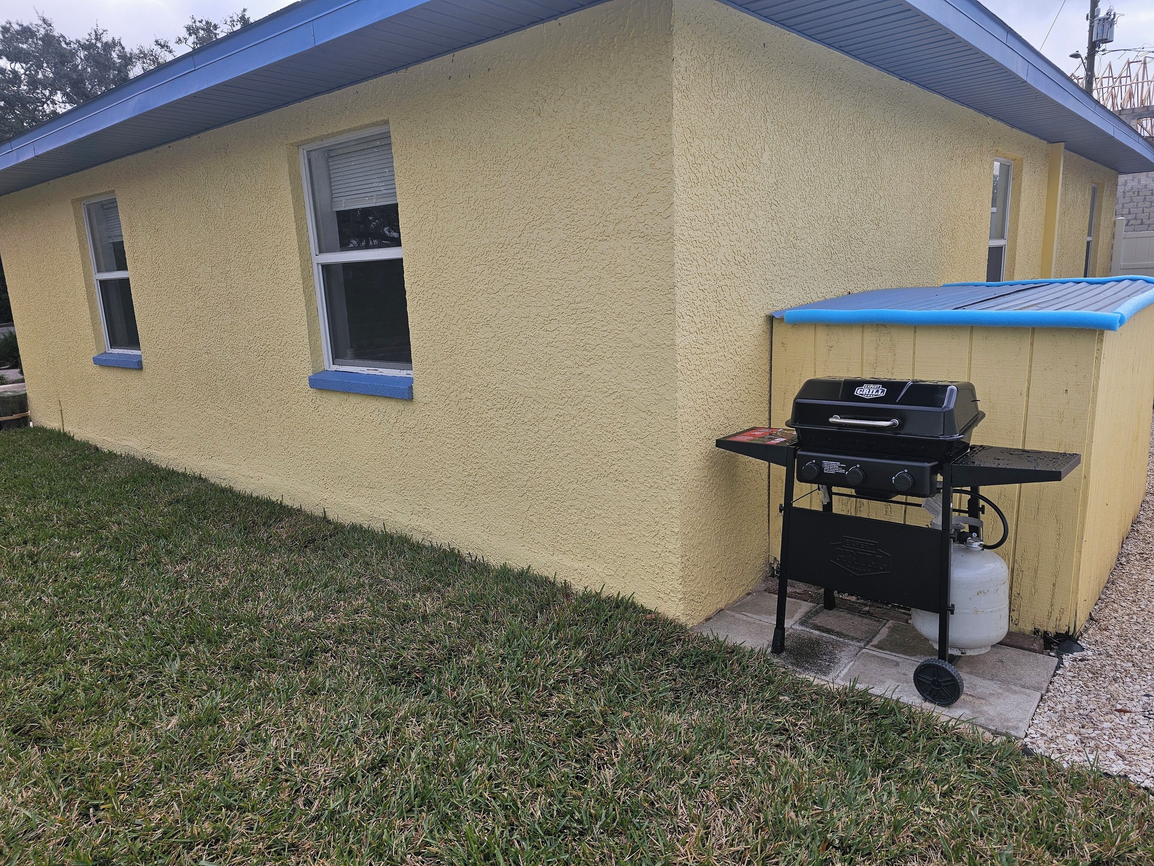 Un bâtiment jaune avec un toit bleu et un barbecue fixé sur le côté.