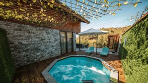 A swimming pool with a wooden deck, a stone wall, and a pergola with climbing plants. - Green Yazıcı Villas (Ardesen)