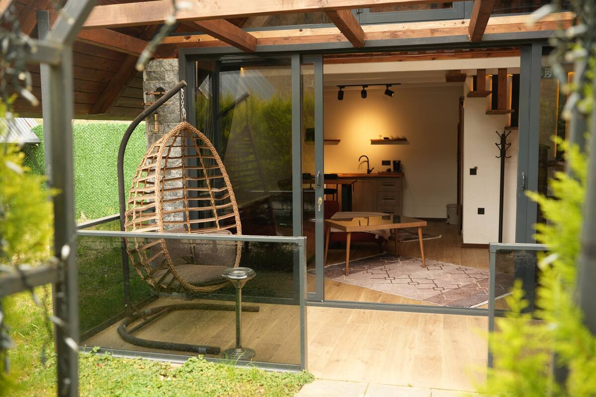 A modern interior with a glass door leading to a kitchen, a hanging chair, and a dining area.