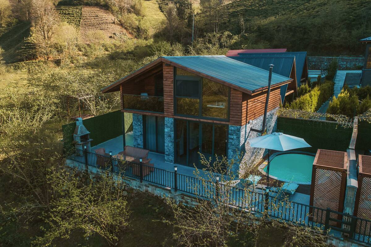 A modern cabin with a balcony, a pool, and a view of the surrounding forest.