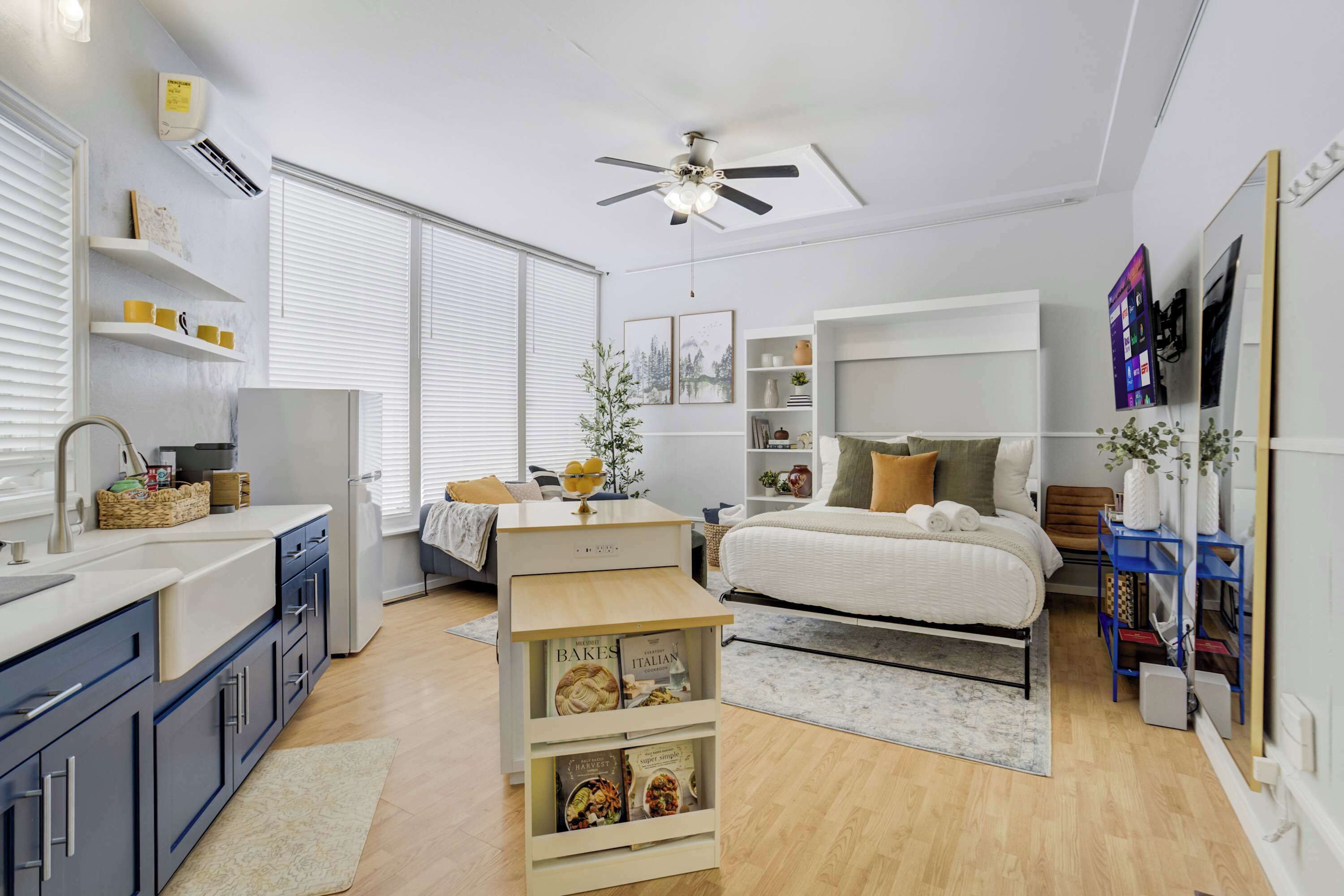 A modern bedroom with a bed, bedside tables, a ceiling fan, and a bookshelf.