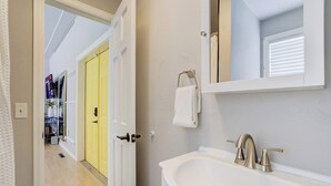 Une salle de bain avec un lavabo blanc, un miroir et une porte jaune.