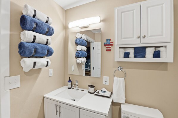 A bathroom with a white sink, mirror, and cabinet, towels hanging on a rack, and a toilet.
