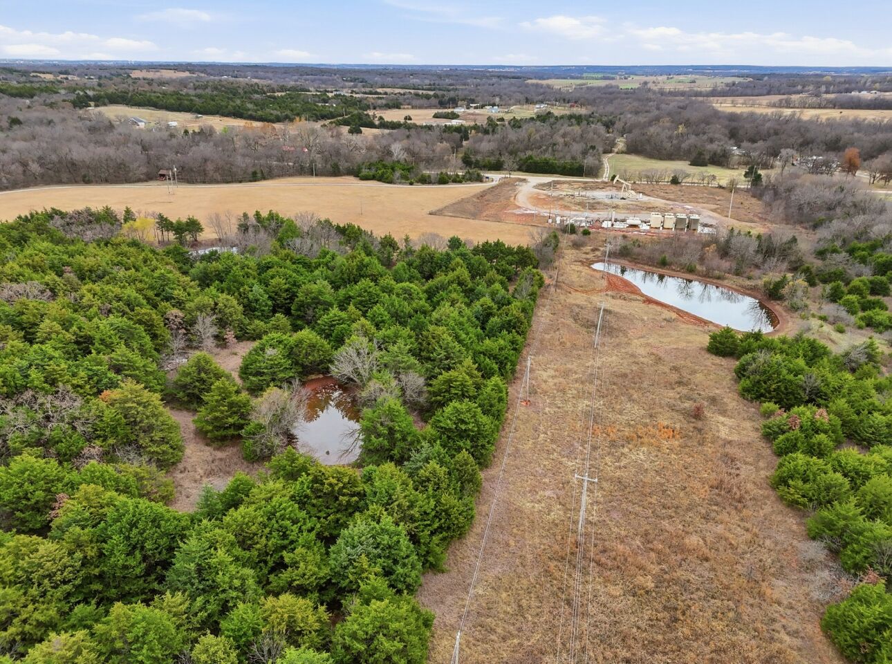 Vista aérea de un paisaje rural con abundante vegetación, un pequeño estanque y un sendero de tierra que lleva a un edificio con techo rojo.