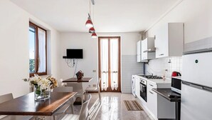 A modern kitchen with a dining area, a TV mounted on the wall, and a washing machine. - Room 'Camera Tripla' with Shared Terrace, Wi-Fi and Air Conditioning (San Zeno)