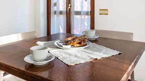 A wooden dining table with a plate of food, two white cups, and a lace table runner. - Room 'Camera Tripla Basic' with Shared Terrace, Wi-Fi and Air Conditioning (San Zeno)