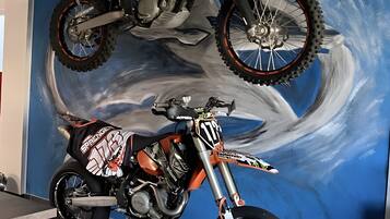 A motorcycle on a lift, a mural with a blue sky and clouds, and a chair in the foreground.
