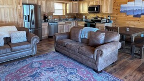 Interior acogedor de una cabaña con paredes de madera, un comedor, una cocina con electrodomésticos modernos y una alfombra grande con diseño.