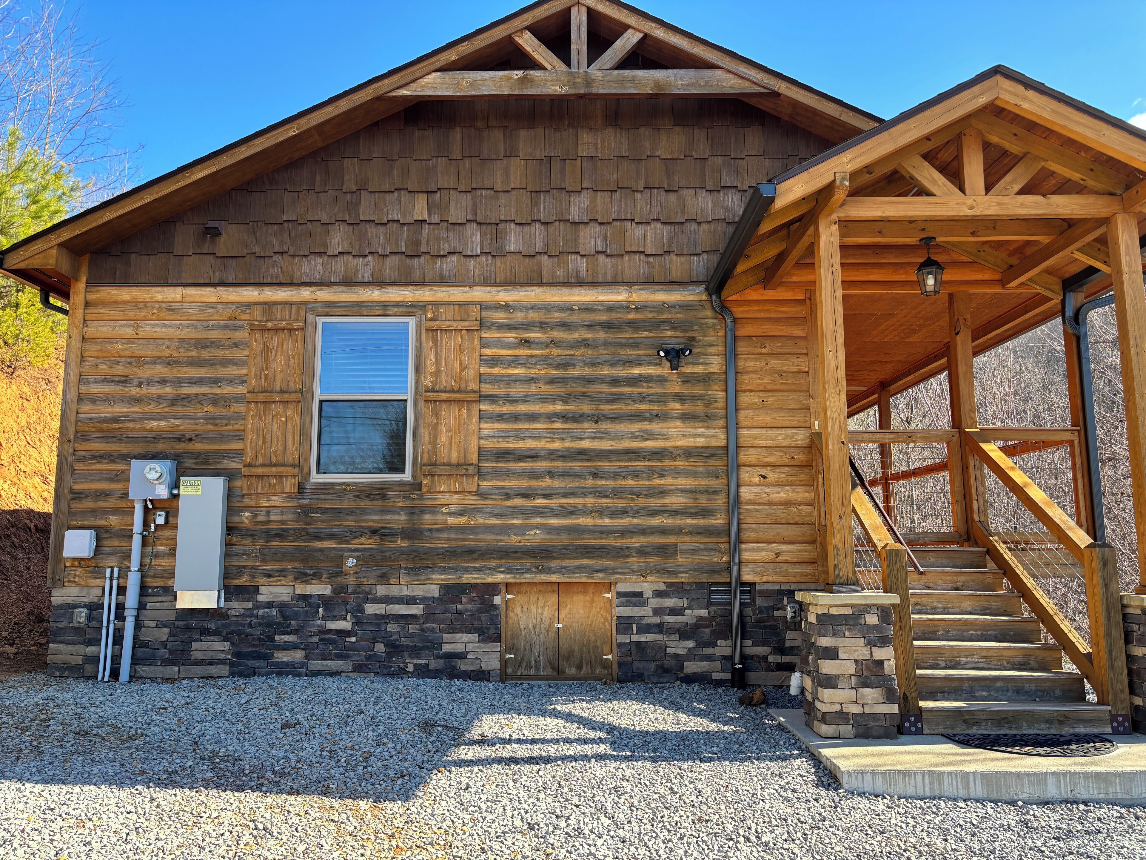 A log cabin with a stone foundation, a wooden porch, and a gravel driveway.