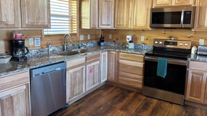 Una cocina moderna con armarios de madera, electrodomésticos de acero inoxidable, encimeras de granito y lavavajillas.