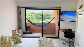 Habitación de hotel con cama, escritorio, silla, televisión y balcón con hamaca.