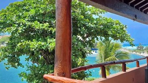 Barana de fusta amb vista a una piscina, vegetació abundant i una vista clara de l'oceà.