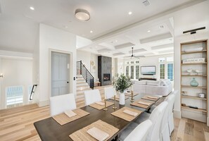 A spacious dining area with a long table, white chairs, and a modern ceiling design. - Seaside Thyme|Private Pool|Steps to Seaside|Golf Cart (Santa Rosa Beach)