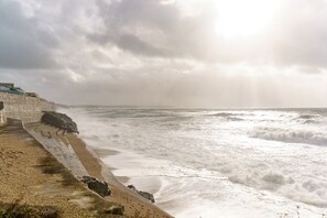 Eine Küstenansicht mit einer Steintreppe, die zum Strand führt, Wellen, die auf die Küste branden, und einem bewölkten Himmel.