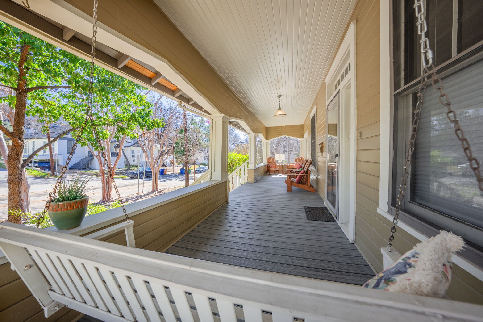 A covered porch with a swing, a potted plant, and a view of the street.