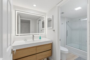 Um banheiro moderno com toucador branco, um espelho grande, box de vidro e vaso sanitário.