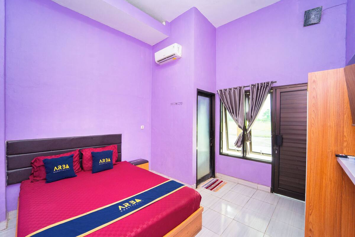 A bedroom with a bed, a wardrobe, a window with curtains, and an air conditioning unit.