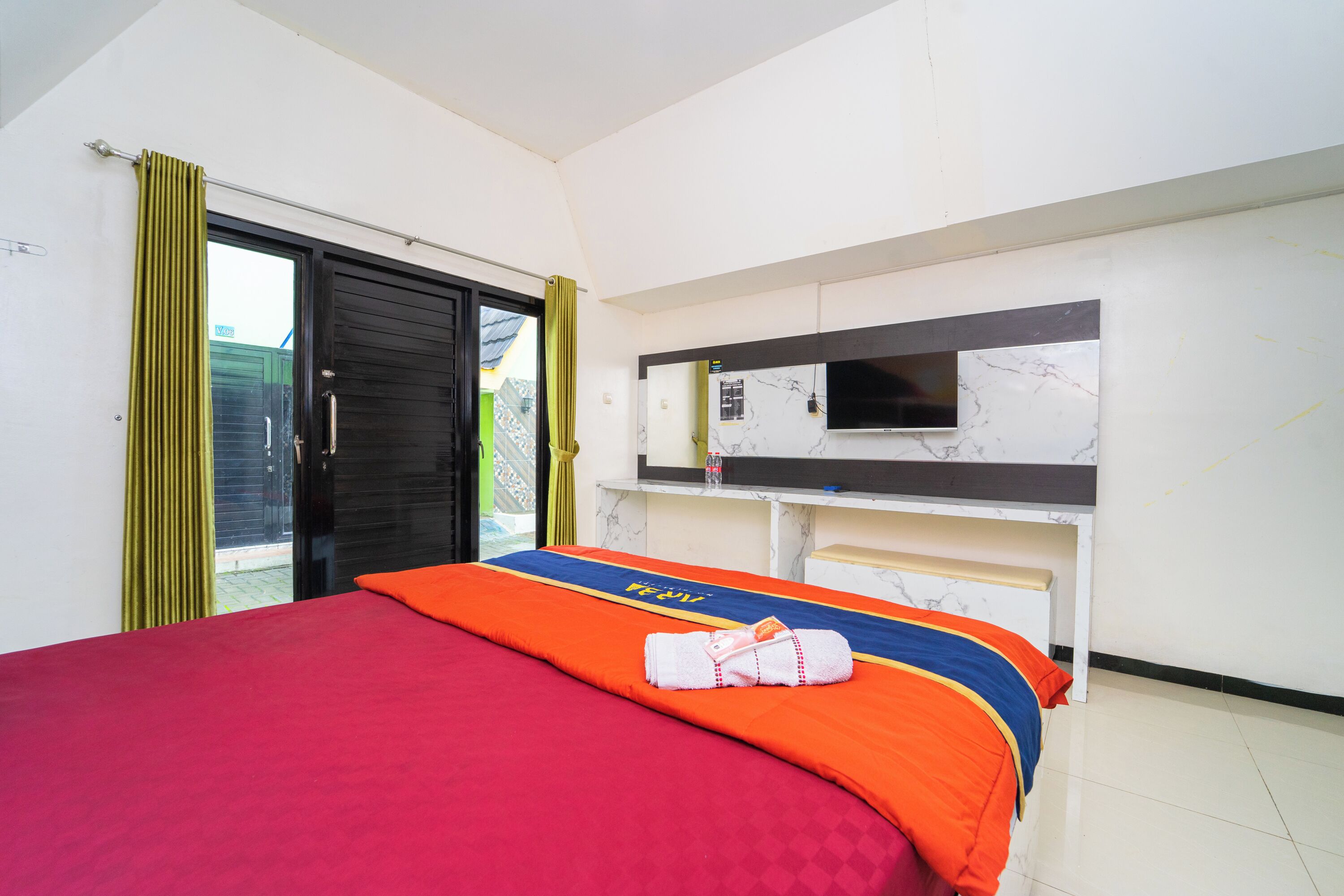 Een hotelkamer met een bed, een aan de muur bevestigde televisie en een schuifdeur.